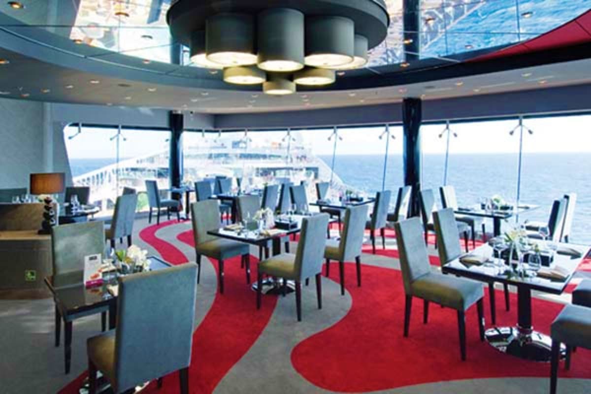 Elegant dining room on MSC Preziosa cruise ship with floor-to-ceiling ocean views, red patterned carpeting, and contemporary 