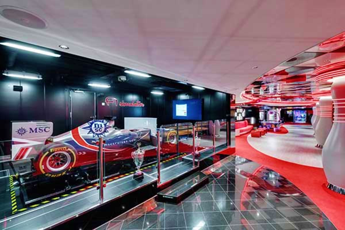 Modern cruise ship entertainment venue with Formula 1 race car display, red neon lighting, and interactive racing simulator a