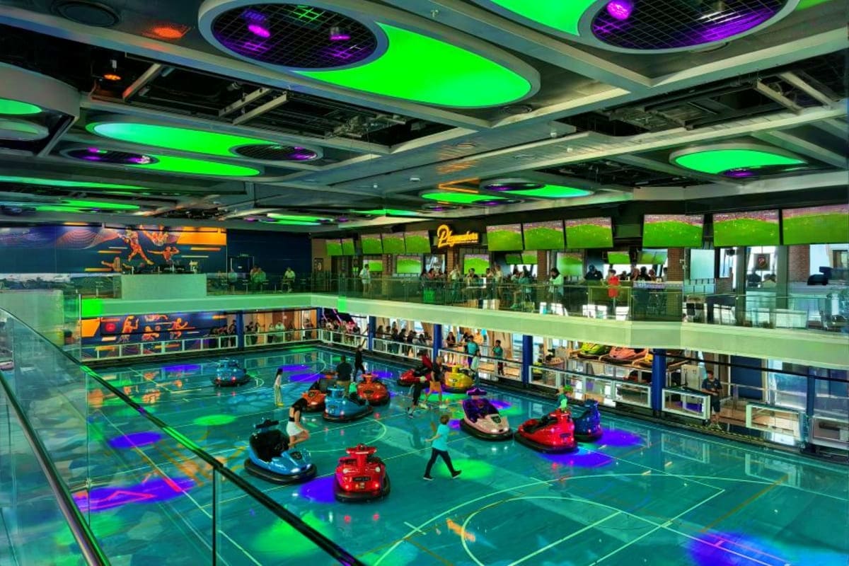 Indoor bumper car arena with neon green and purple lighting on ceiling, colorful bumper cars on turquoise floor, and multi-le