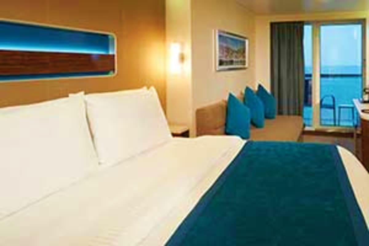 Norwegian Breakaway New England Escape Modern cruise ship stateroom with ocean view balcony, queen bed with white linens, teal accents, and seating area overlooking