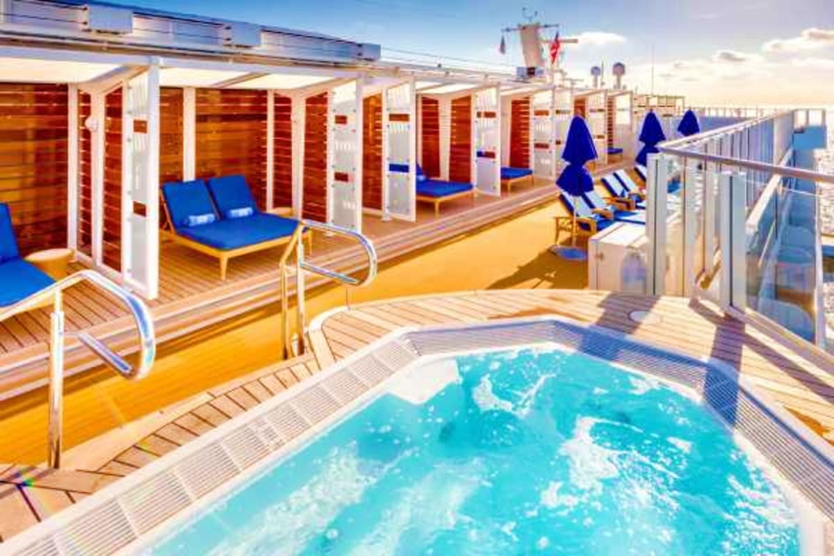 Norwegian Breakaway New England Escape Cruise ship deck with swimming pool, private cabanas with blue lounge chairs, and wooden deck furniture under sunny skies