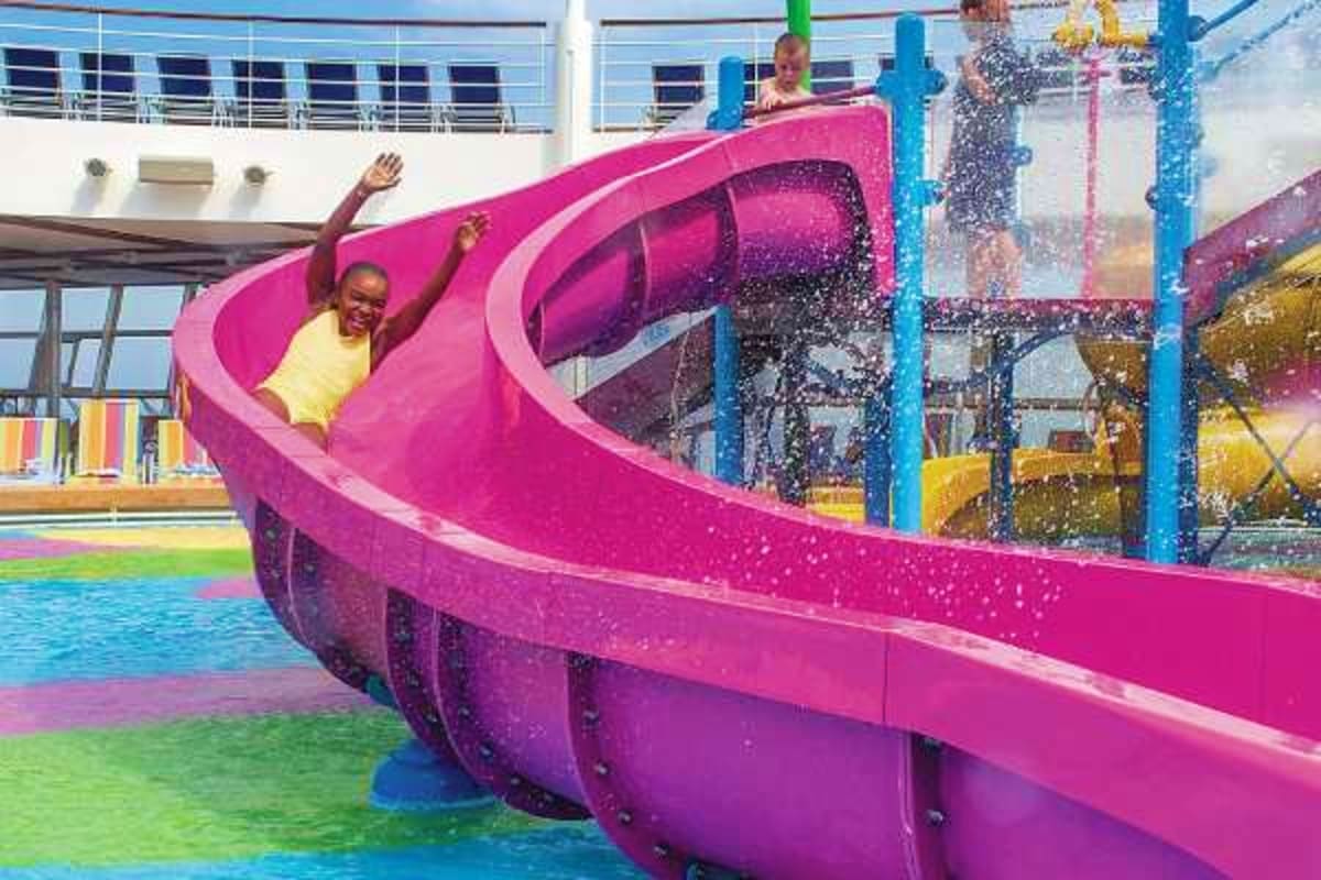 Child sliding down pink waterslide with arms raised on Oasis of the Seas cruise ship pool deck