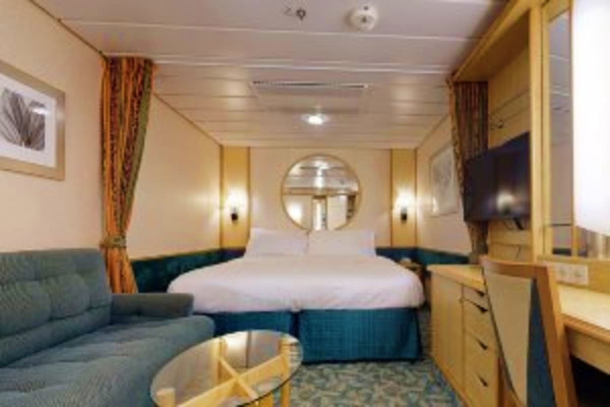Luxurious cruise ship cabin with queen bed, sofa, round mirror, wood paneling, and ocean view porthole on Independence of the
