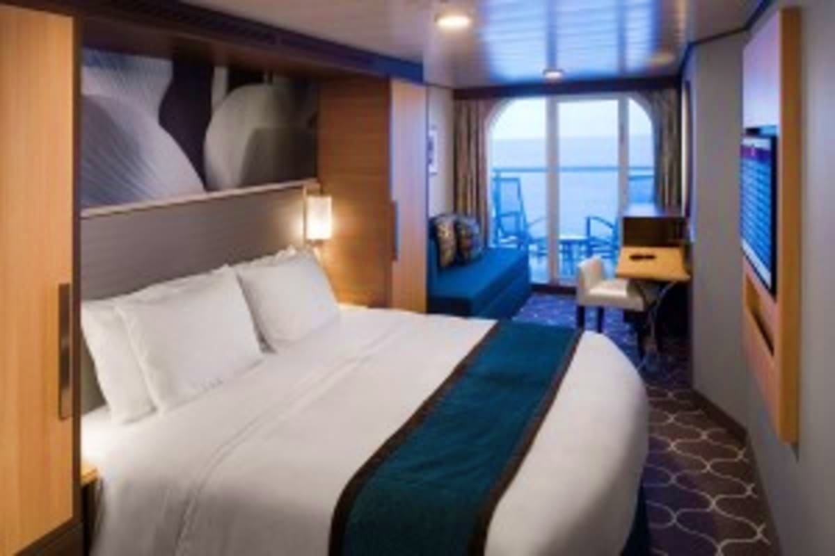 Luxury cruise ship cabin with queen bed, ocean view balcony, sitting area, and modern furnishings overlooking the sea