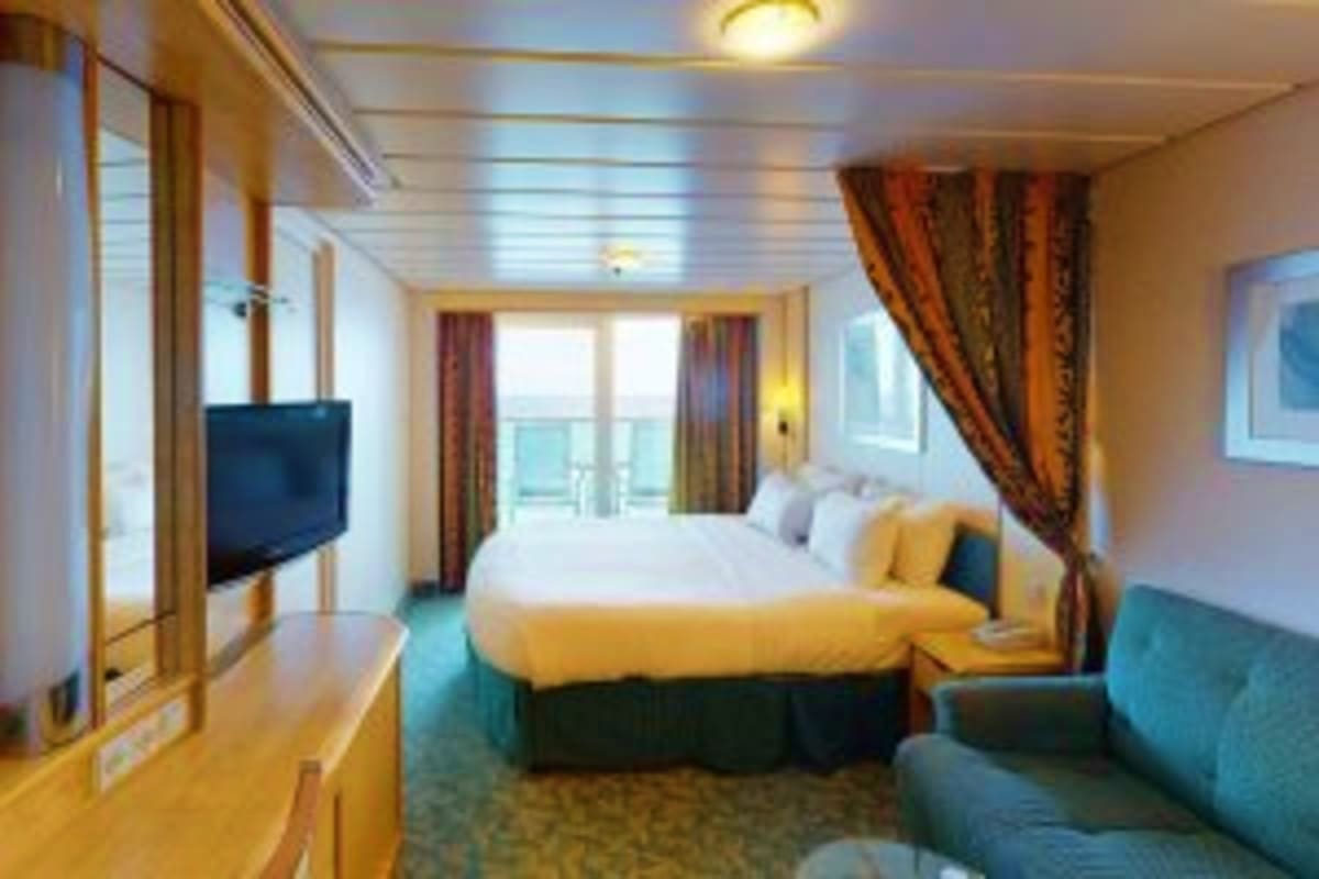 Spacious cruise ship cabin with queen bed, flat-screen TV, sofa, and ocean view balcony with curtains