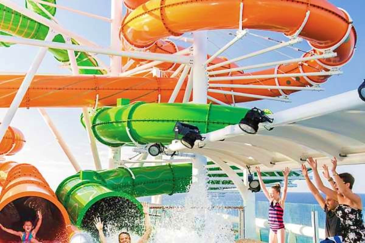 Water slide complex on cruise ship with green and orange slides, passengers enjoying splash zones and ocean view in backgroun