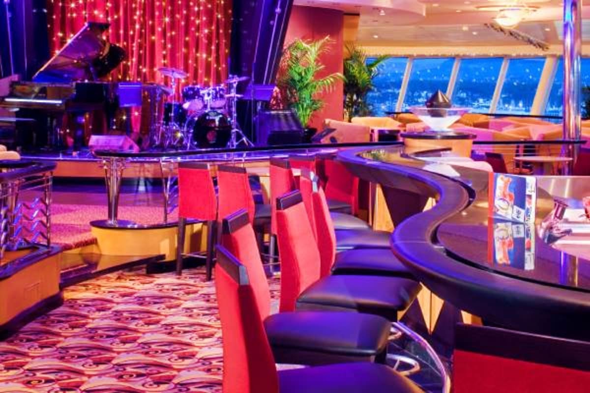 Modern cruise ship entertainment venue with red and black seating, stage with musical instruments, neon lighting, and ocean v