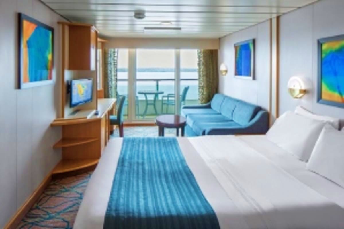 Spacious cruise ship stateroom with ocean view balcony, queen bed, sofa seating area, and modern amenities overlooking the se