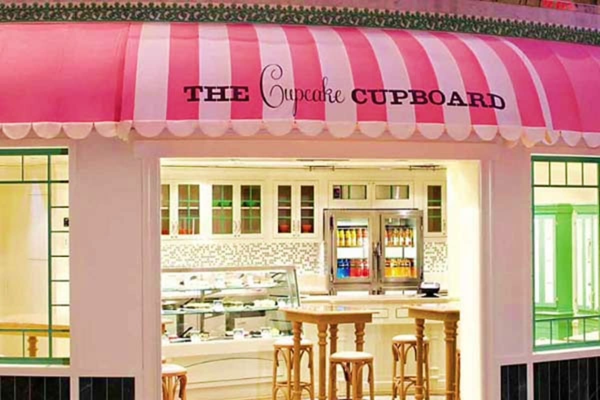 The Cupcake Cupboard storefront with pink and white striped awning, display cases, and wooden bar seating