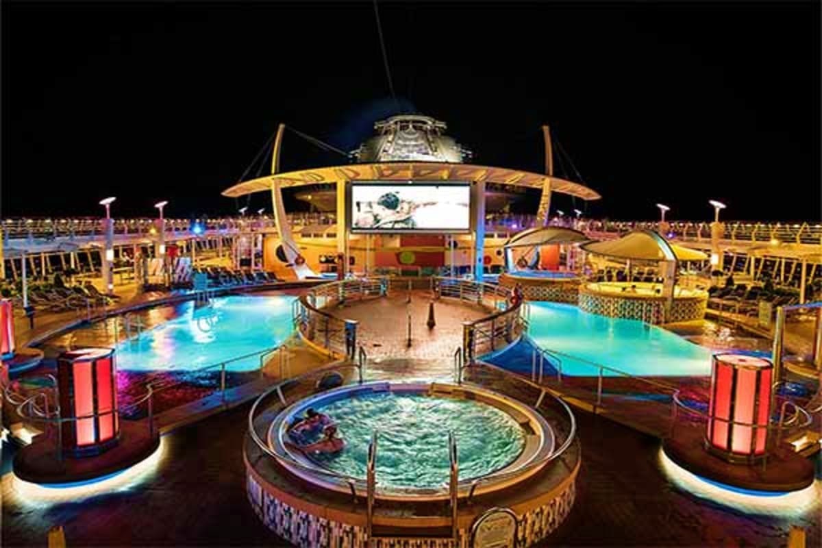 Nighttime view of Vision of the Seas pool deck with illuminated hot tubs, swimming pools, and yellow canopy structures under 