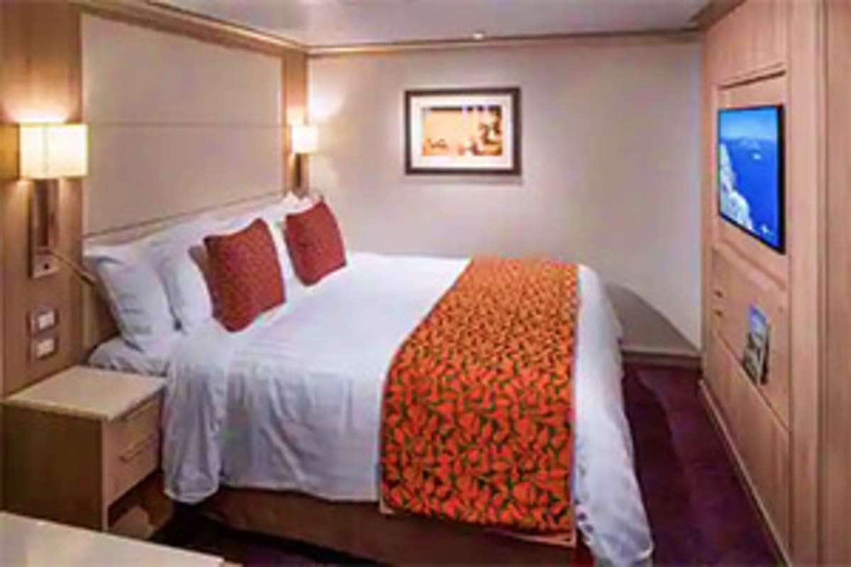 Nieuw Statendam Norway Voyage Modern cruise ship cabin with queen bed, white linens, red decorative pillows and runner, flat-screen TV, wall sconces, and f