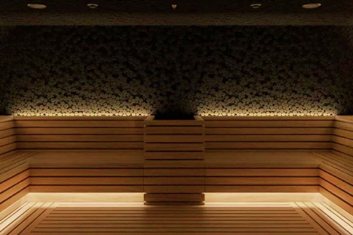 Norwegian Aqua Bermuda Escape Modern sauna interior with wooden bench seating, stone accent wall, and warm ambient lighting