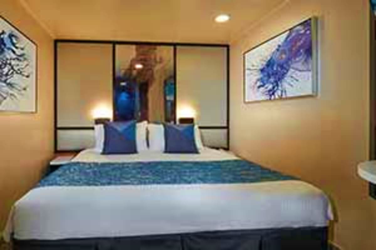 Norwegian Jade Japan Cruise Modern cruise ship cabin with queen bed, blue accents, mirrored wardrobe, and framed artwork on beige walls