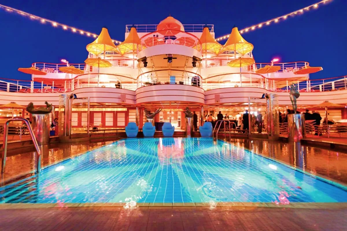 Illuminated outdoor swimming pool on Costa Fascinosa cruise ship at night with castle-like superstructure and golden tower li