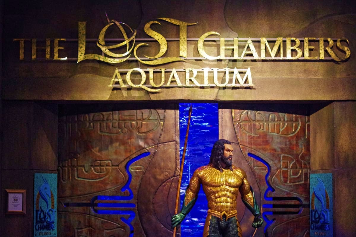 The Lost Chambers Aquarium entrance with golden Aquaman statue holding a trident under ornate bronze archway and blue water b