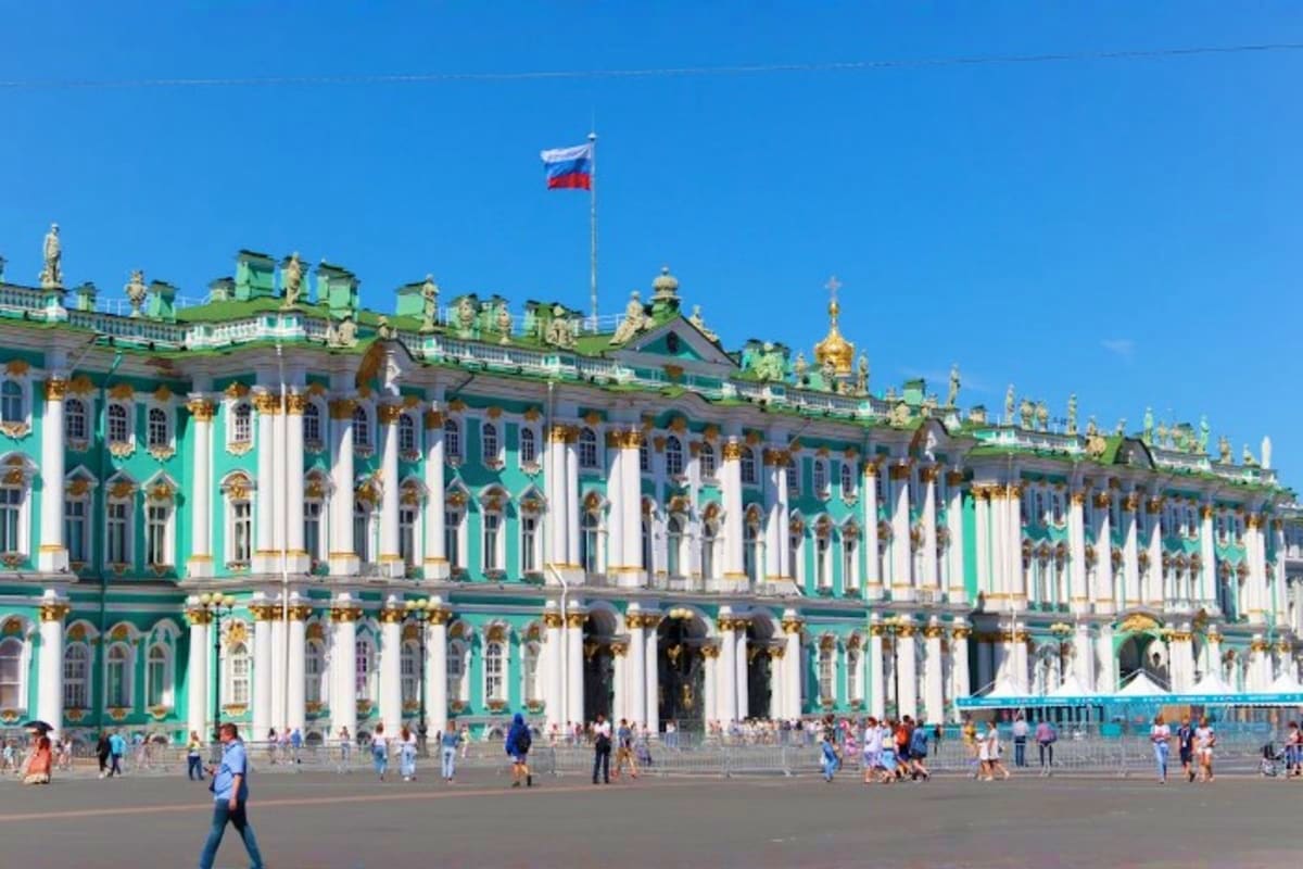 Winter Palace in St. Petersburg with turquoise and white facade, golden domes, Russian flag, and tourists in Palace Square un