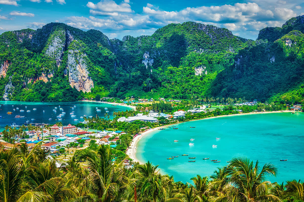 Aerial view of Phi Phi Islands in Phuket with turquoise water, limestone cliffs, palm trees, sandy beaches and moored boats