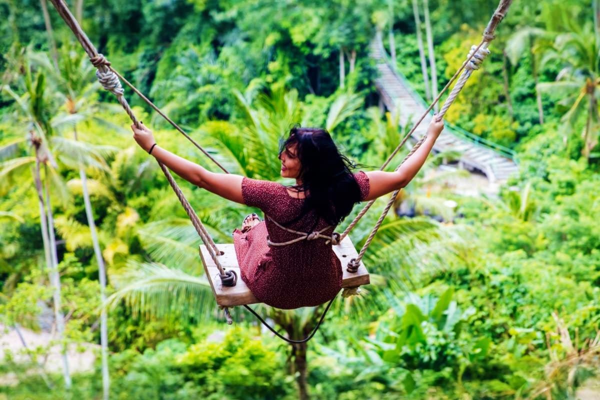 Woman on jungle swing with arms raised above lush tropical forest canopy in Bali