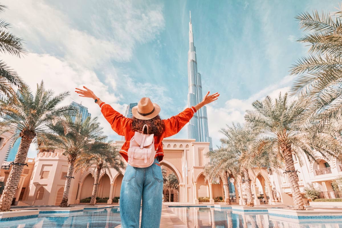 Tourist with arms raised in celebration at Dubai courtyard with Burj Khalifa and palm trees in background