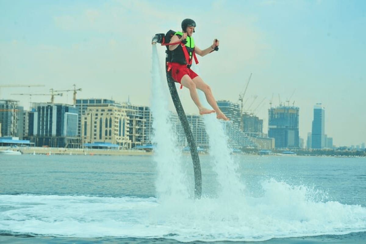 Person flyboarding above ocean waves with city skyline and high-rise buildings in background