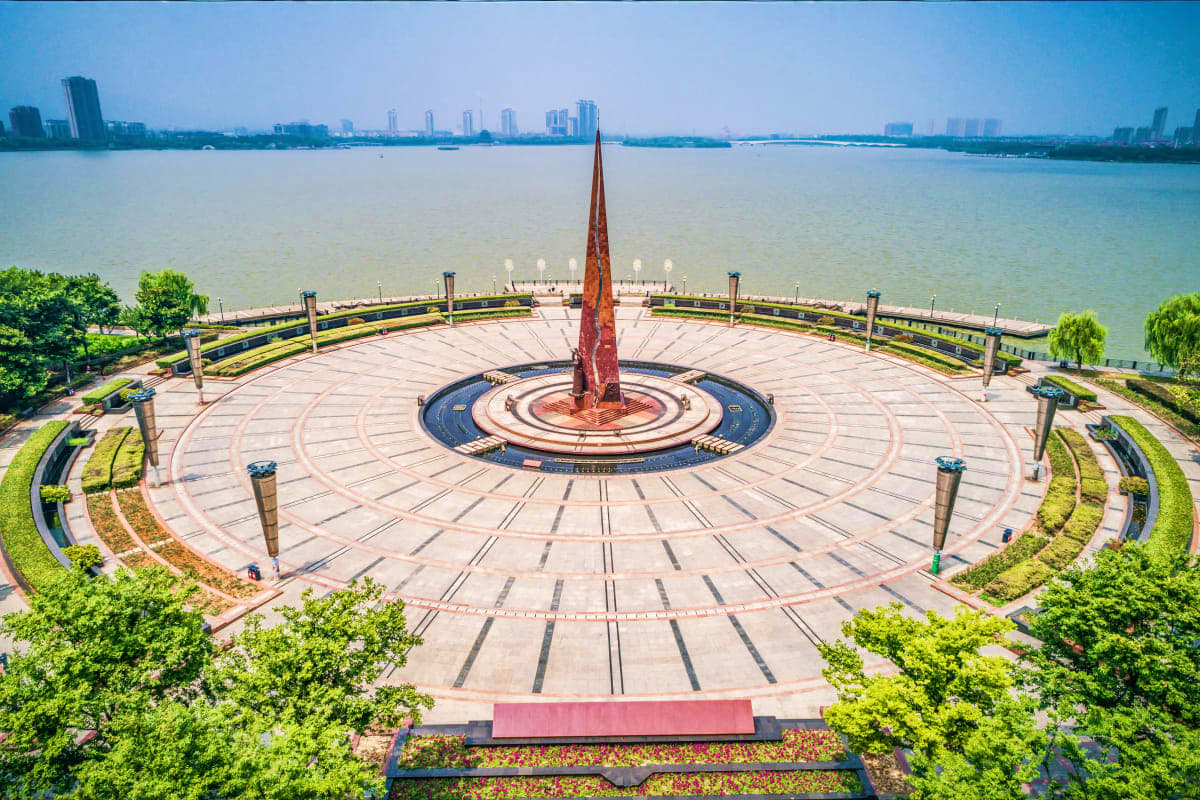Aerial view of Tashkent's Independence Square with central red monument, waterfront promenade, and city skyline across the ri