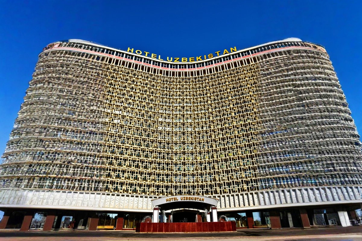 Explore Uzbekistan Hotel Uzbekistan building with curved cylindrical architecture and yellow signage against clear blue sky in Tashkent