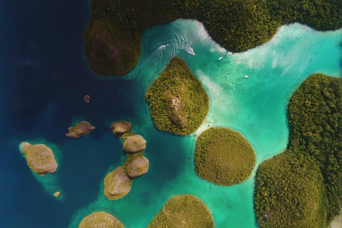 Aerial view of turquoise lagoon surrounded by dense forest and rocky islands in Bali, Indonesia with boats anchored in shallo