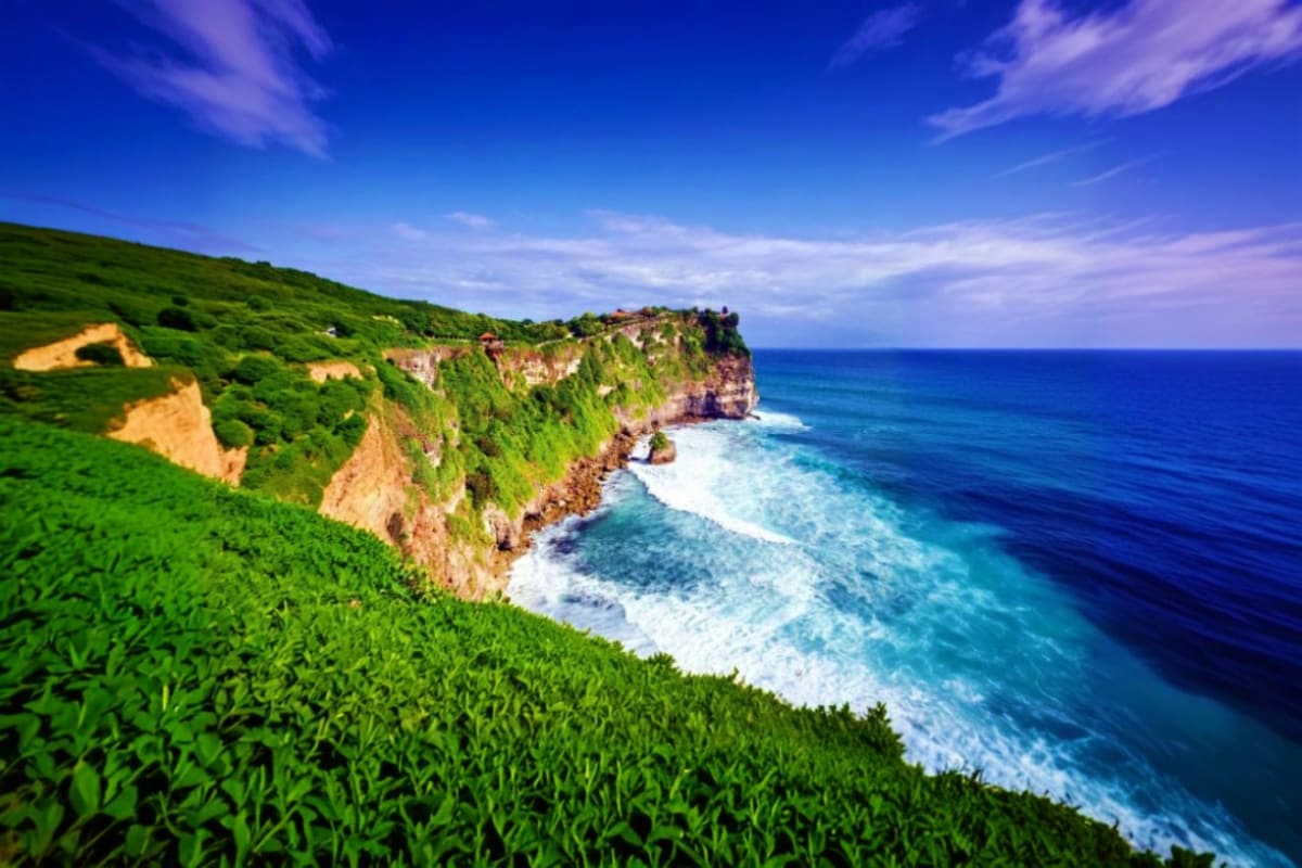 Dramatic coastal cliffs with green vegetation overlooking turquoise ocean waves and white sandy beach in Bali, Indonesia