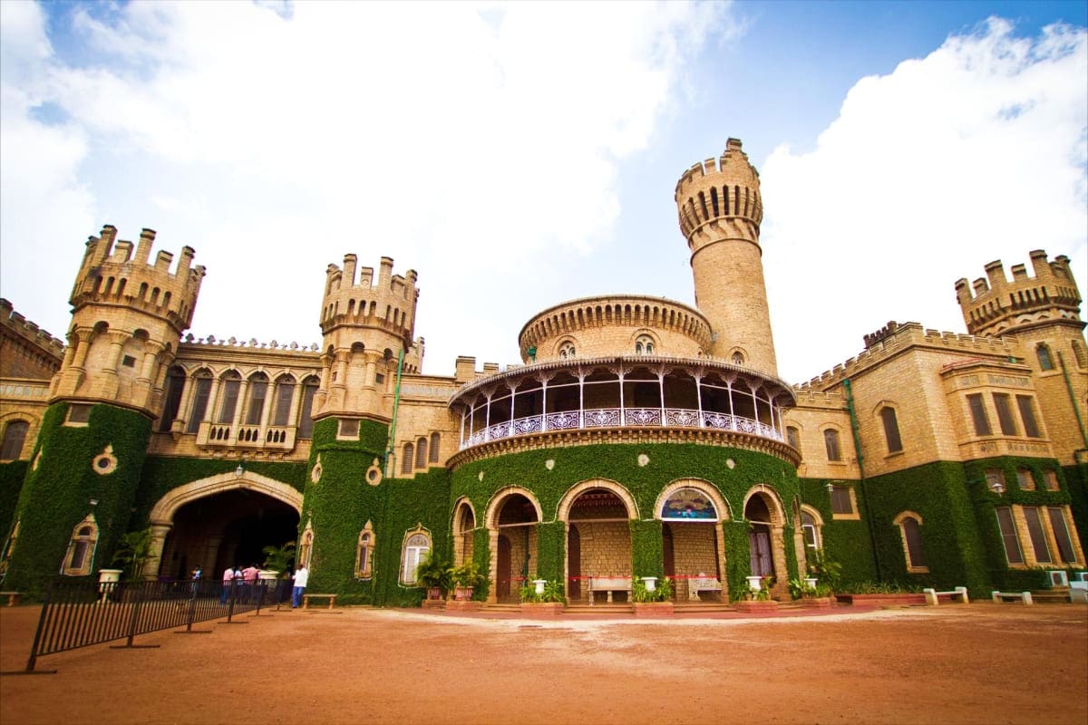 South India Discovery Hills and Heritage Getaway Bandipur Palace with crenellated towers, ivy-covered walls, and minaret under blue sky, reflecting South Indian heritage arch