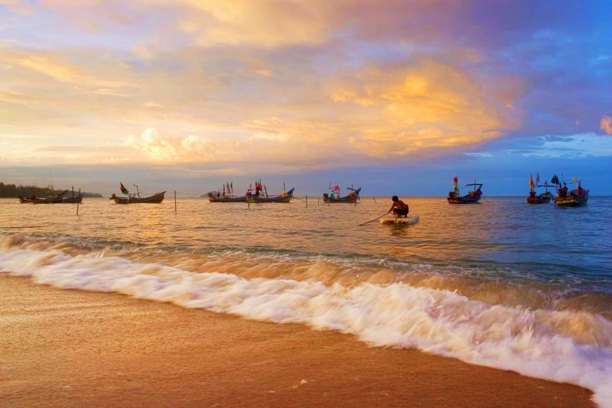 Fishing boats anchored in shallow waters at sunset on a tropical beach with golden sky and waves rolling onto sandy shore