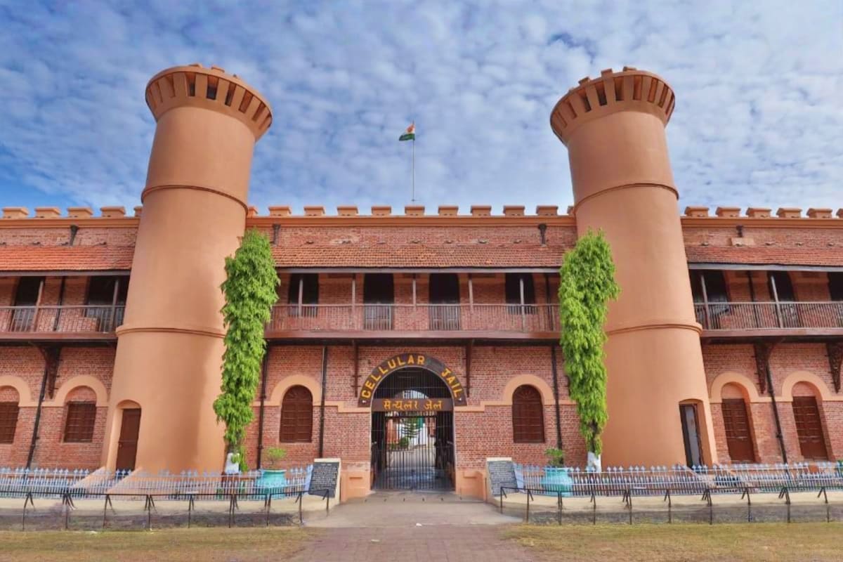 Historic red brick fort with two cylindrical towers and Indian flag, featuring crenellated walls and ivy-covered columns