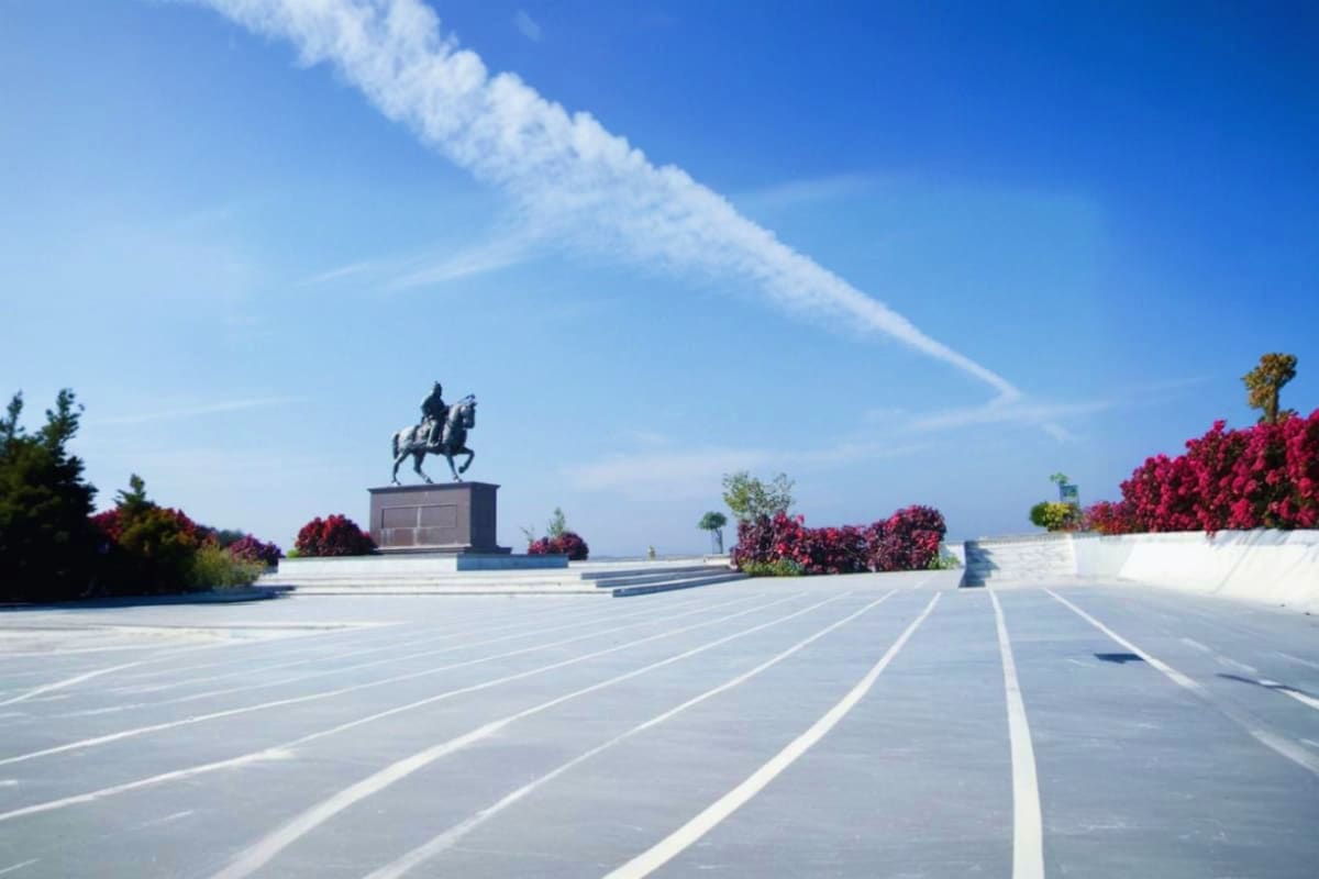 Equestrian statue monument on wide plaza with magenta bougainvillea flowers and blue sky with contrails