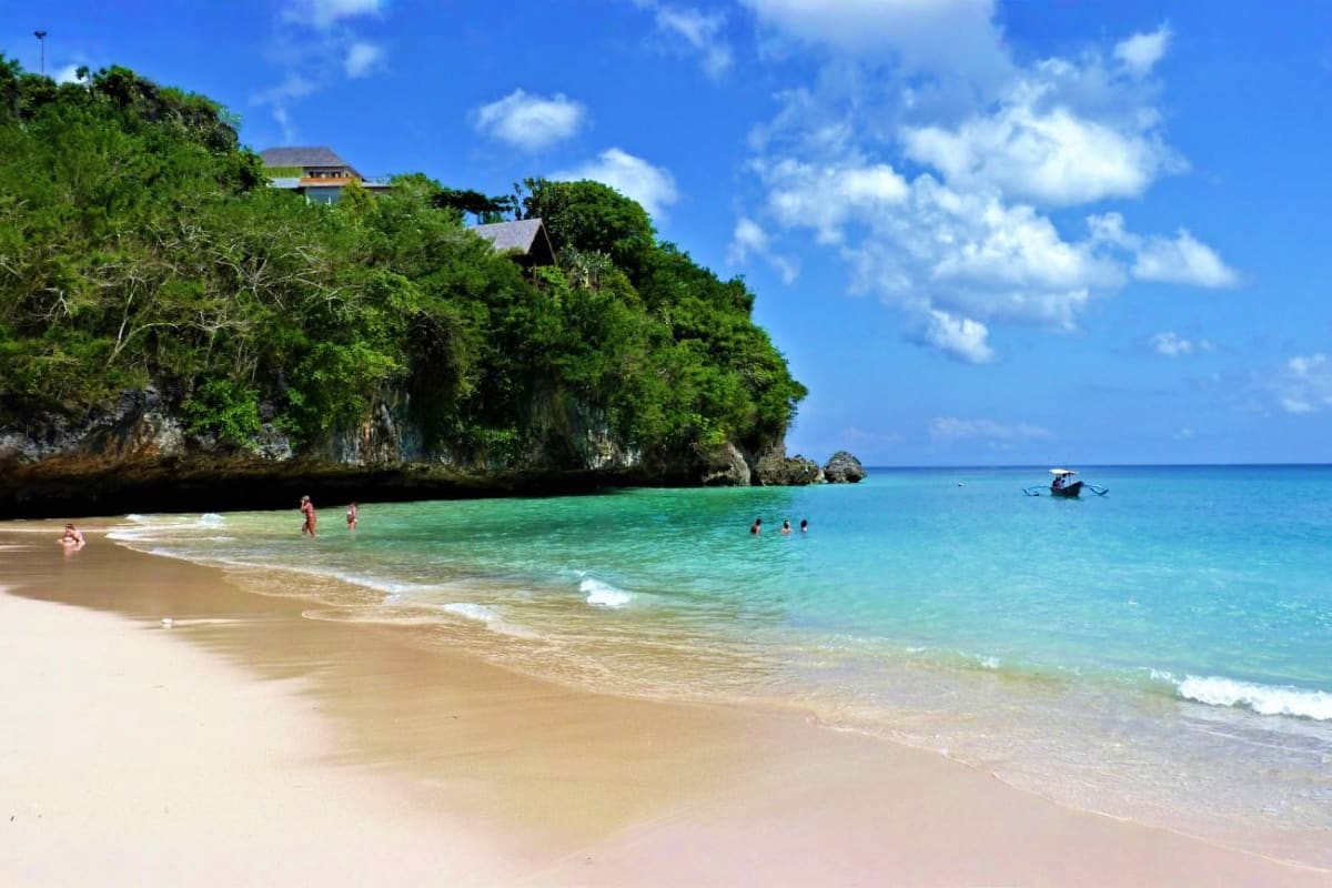 Tropical beach cove in Bali with turquoise water, white sand, limestone cliffs, beachfront villa, and swimmers in the ocean