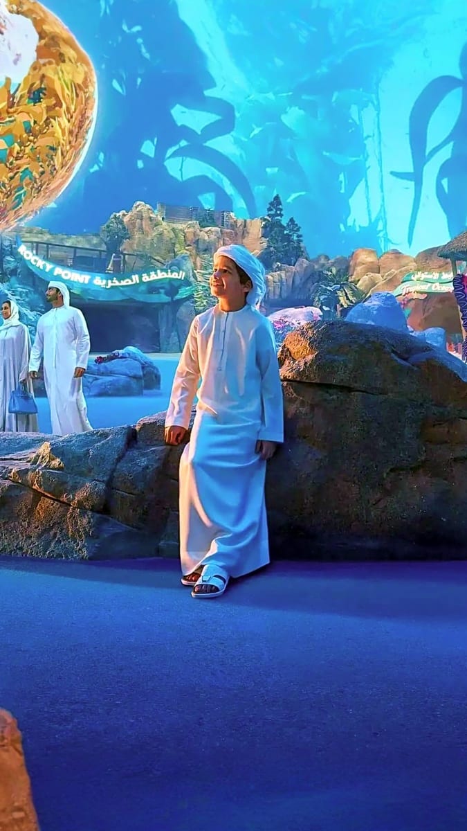 Young man in traditional white thobe and blue cap at Sheikh Zayed Grand Mosque-inspired exhibition in Abu Dhabi with architec