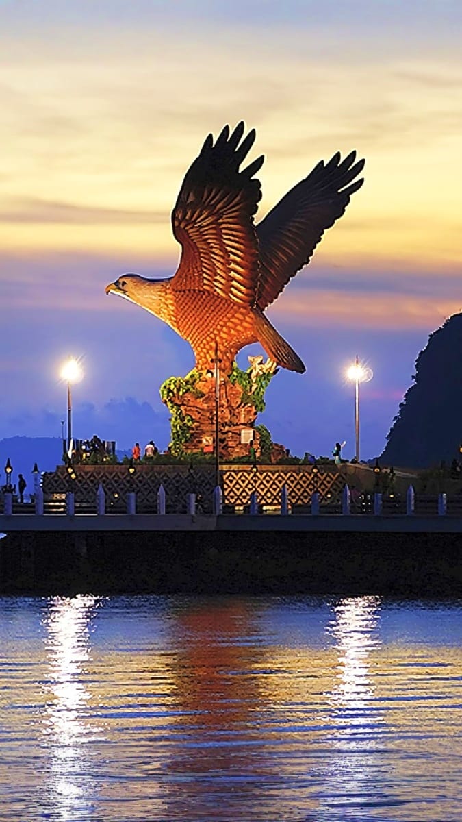 Langkawi Eagle Square monument illuminated at dusk with golden eagle statue overlooking waterfront and mountains