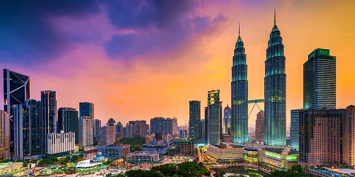 Kuala Lumpur skyline at sunset with Petronas Twin Towers illuminated against purple and golden sky