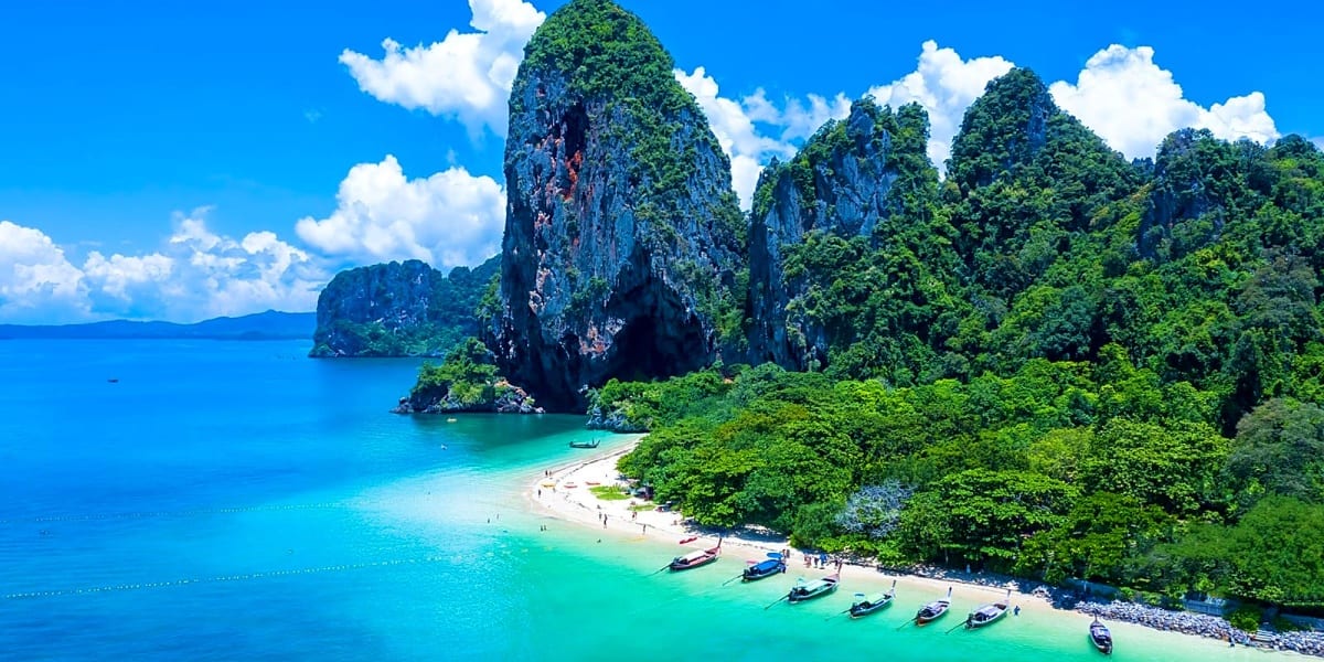 Emerald lagoon surrounded by towering limestone cliffs with dense tropical vegetation and longtail boats on turquoise water i