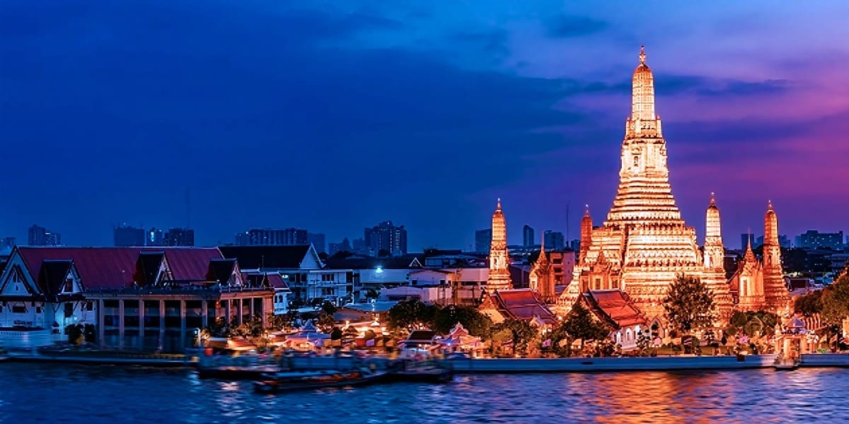 Wat Arun temple illuminated at twilight reflected in the Chao Phraya River, Bangkok skyline in background