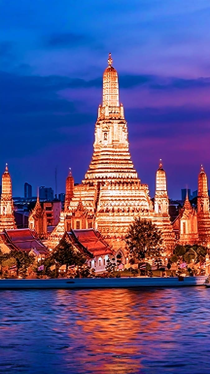 Illuminated Wat Arun temple reflected in the Chao Phraya River at twilight in Bangkok, Thailand