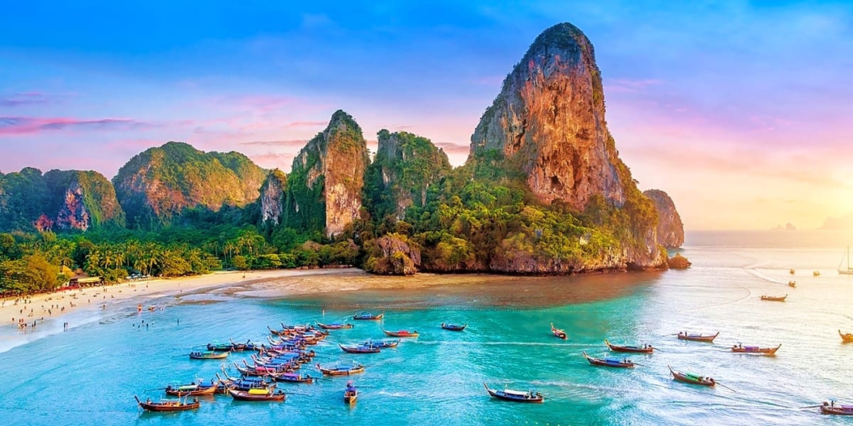 Limestone cliffs and turquoise waters of Railay Beach in Phuket with traditional longtail boats and sandy shore at sunset