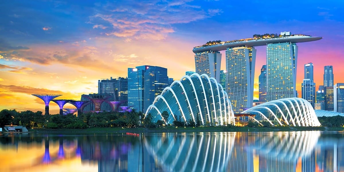 Singapore skyline at sunset with Marina Bay Sands hotel and illuminated Supertree Grove reflected in calm water
