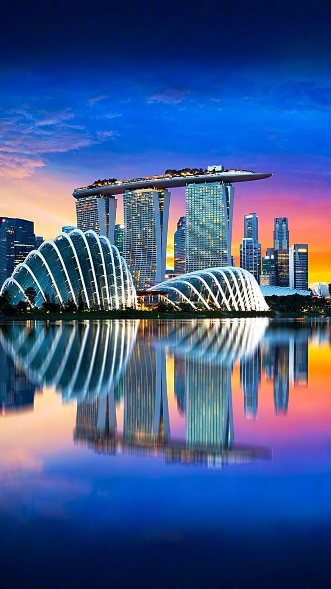 Marina Bay Sands hotel and Supertree Grove lit up at sunset with reflections in still water, Singapore skyline