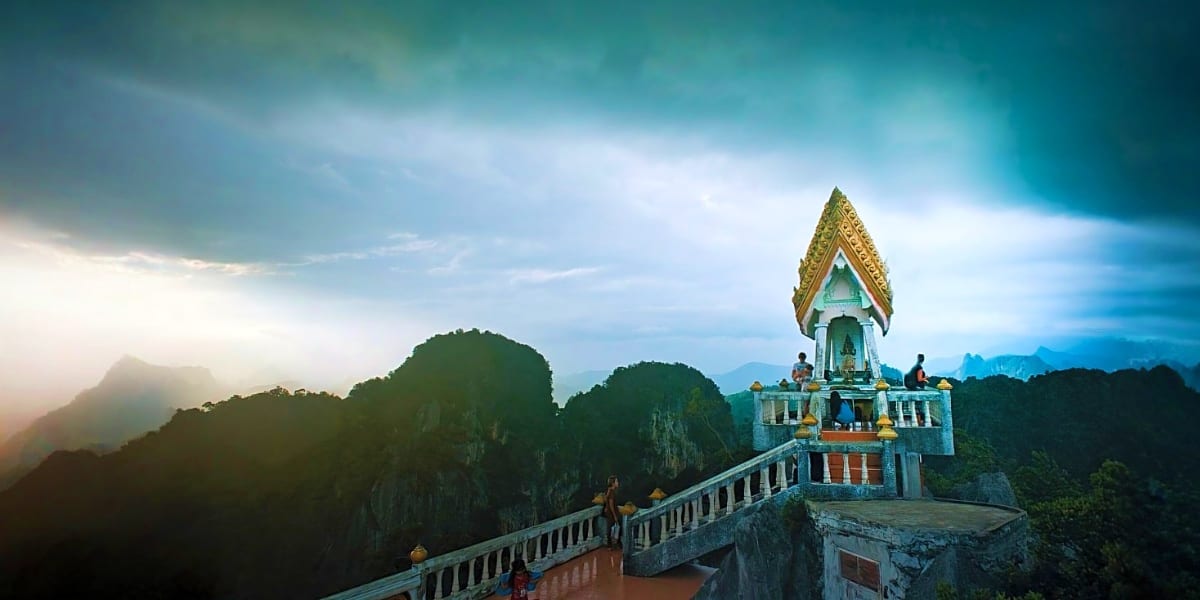 Buddhist temple with golden spire perched on cliff overlooking limestone mountains in Krabi, Thailand