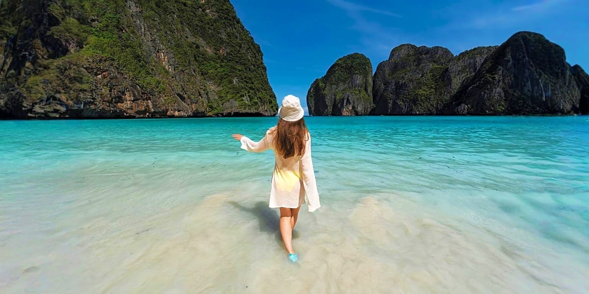 Woman wading in turquoise water toward limestone cliffs in tropical island bay