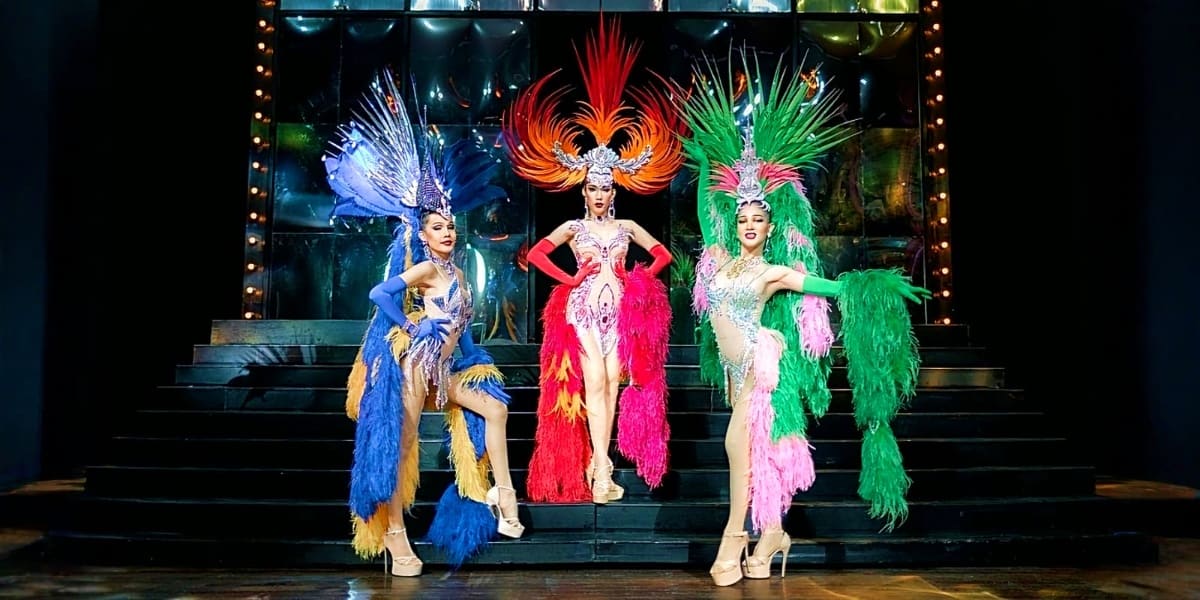 Three performers in elaborate feathered headdresses and sequined costumes on stage at Alcazar Cabaret Show