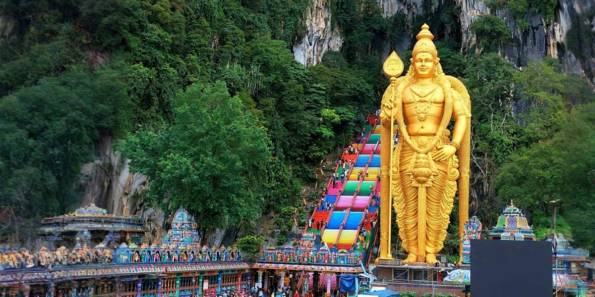 Giant golden Lord Murugan statue at Batu Caves entrance with colorful staircase and limestone cliffs in Malaysia