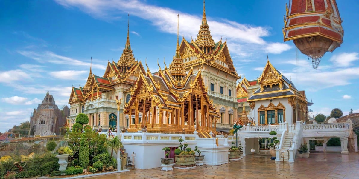 Wat Traimit Golden Buddha Temple in Bangkok with ornate golden spires and white marble platform under blue sky