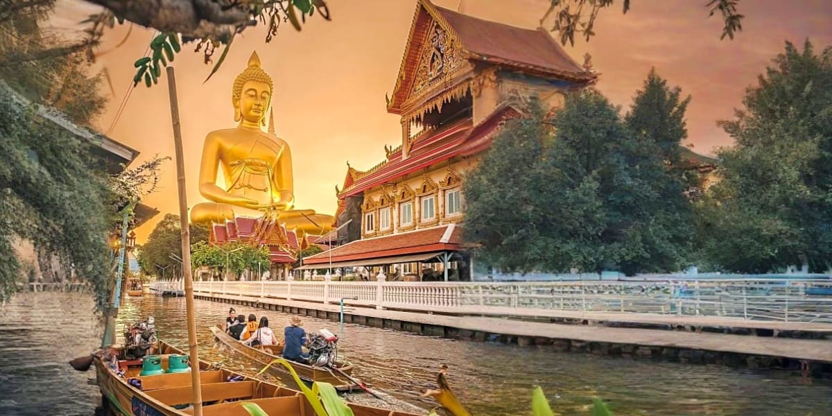 Golden Buddha statue overlooking traditional Thai temple and wooden longtail boat on canal at sunset