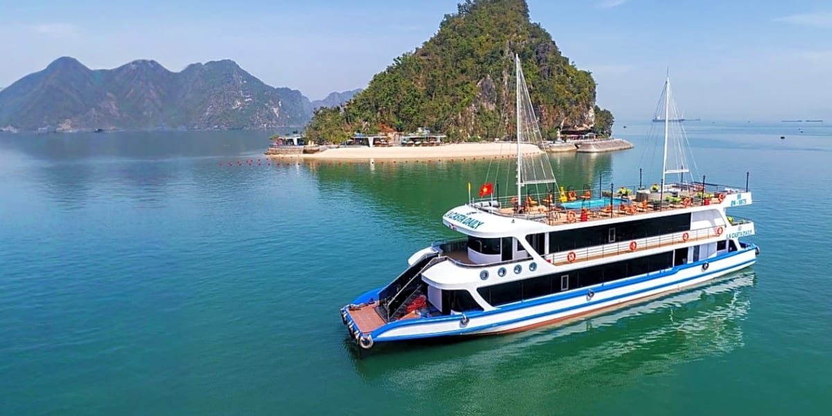 Luxury sailboat with blue stripe moored in Halong Bay turquoise waters, limestone karst mountains and forested island in back