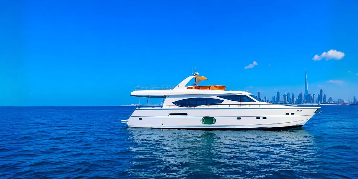 Luxury white and gold motor yacht anchored in blue ocean waters with Dubai skyline visible in background
